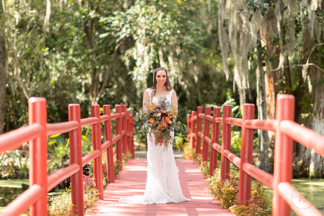 Bride holds her bouquet in the middle of the red bridge at Magnolia Plantation