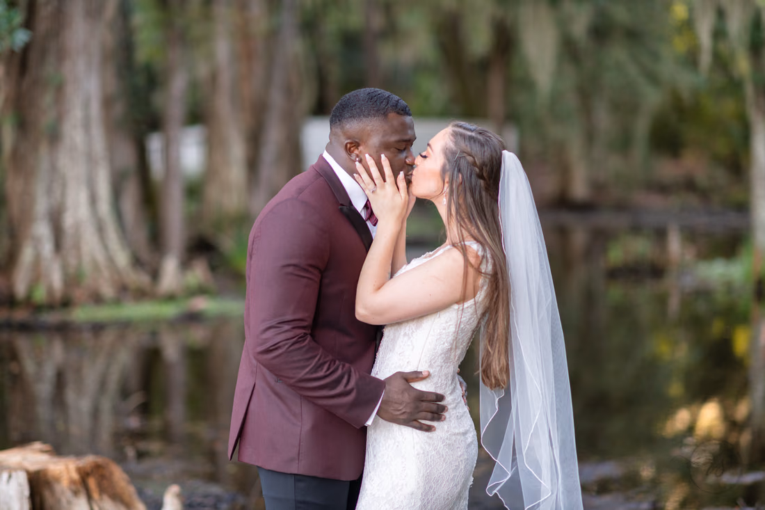 Bride holds the groom's face for a kiss by the water at Magnolia Plantation