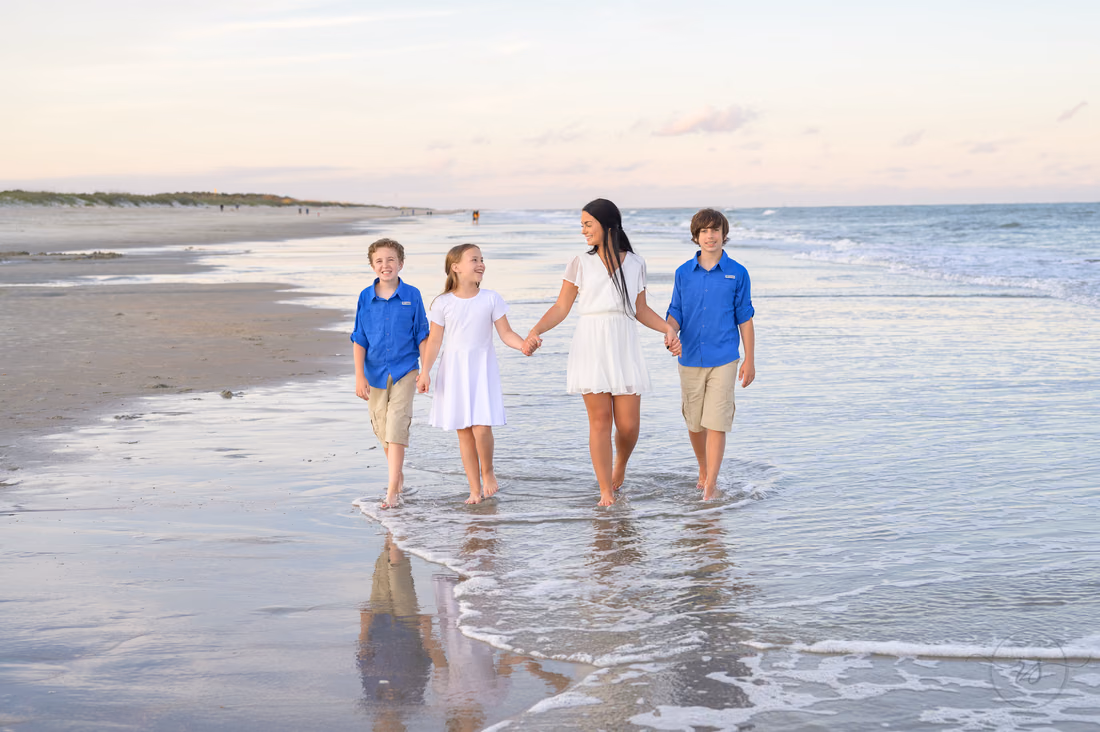 Siblings walk hand in hand through the shallow water at sunset at Huntington Beach State Park