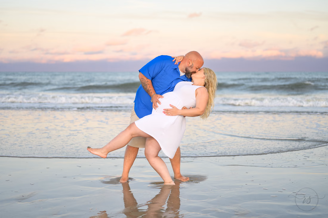 He dips his pregnant fiancée back for a kiss in the surf at Huntington Beach State Park