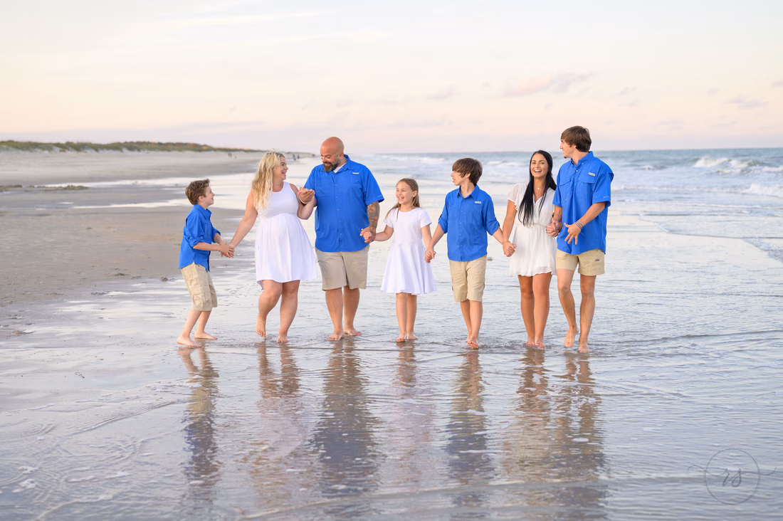 Family smiles as they walk together in the ocean at sunset at Huntington Beach State Park