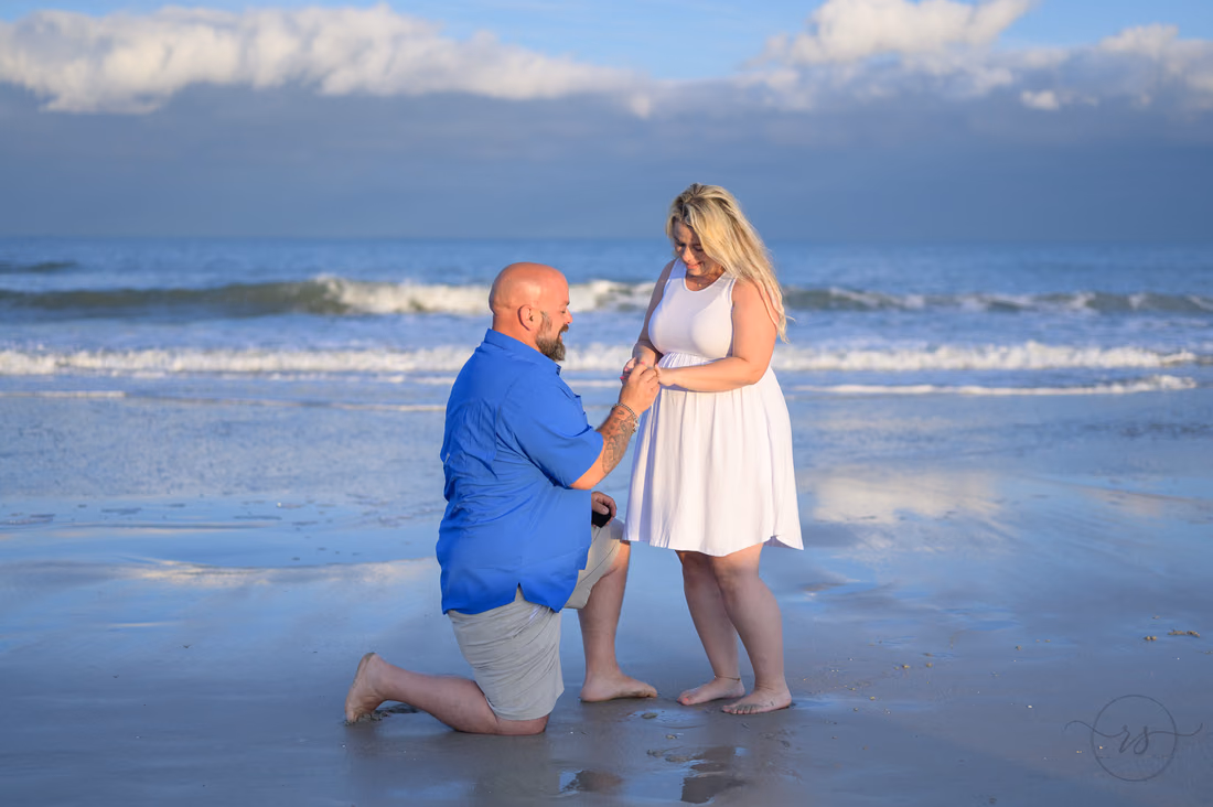 Kneeling on the beach, he slips the ring on her finger at Huntington Beach State Park