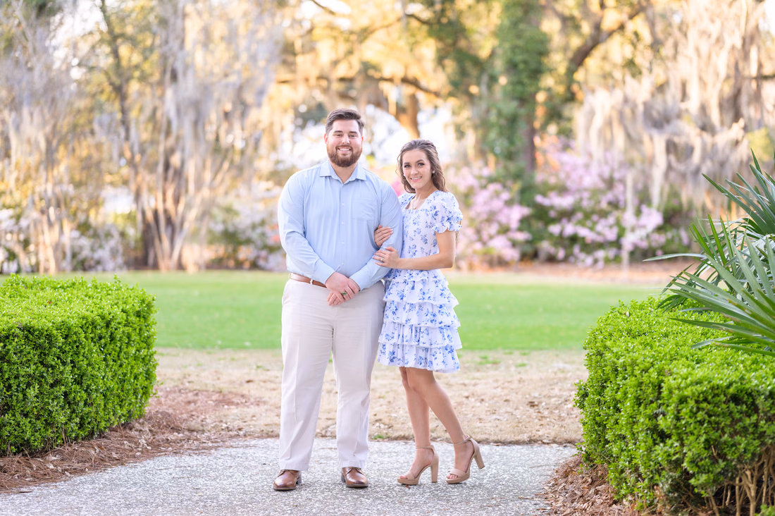 Engaged couple arm in arm on a garden path lined with hedges at Caledonia Golf and Fish Club