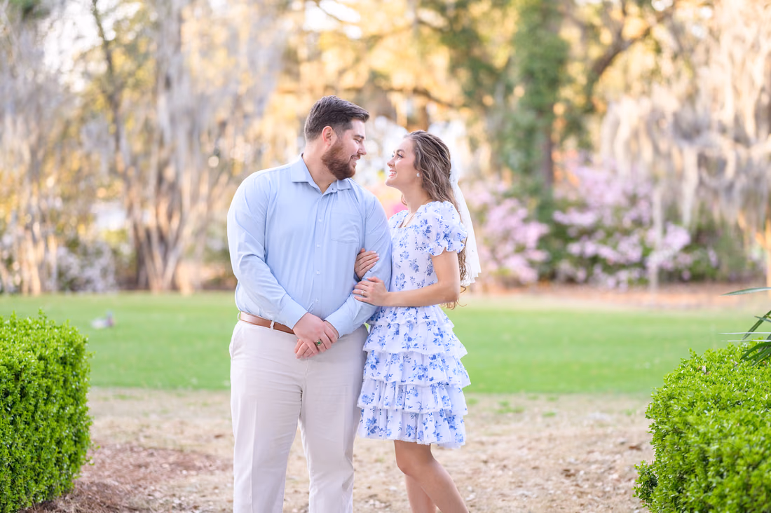 Couple smiling at each other between boxwood hedges and spring azaleas at Caledonia Golf and Fish Club