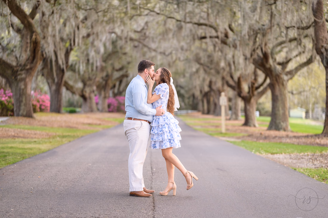 Couple kissing on the oak-lined road with azaleas behind at Caledonia Golf and Fish Club