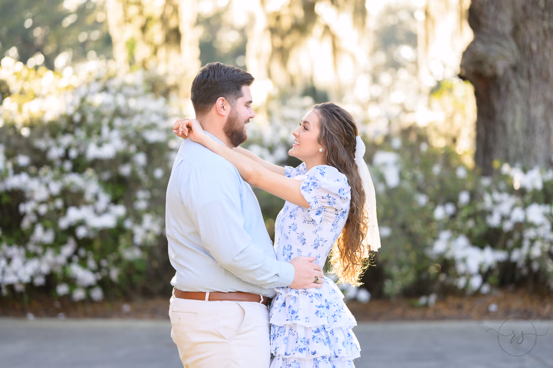 Couple laughing face to face, her arms around his neck, by white azaleas at Caledonia Golf and Fish Club