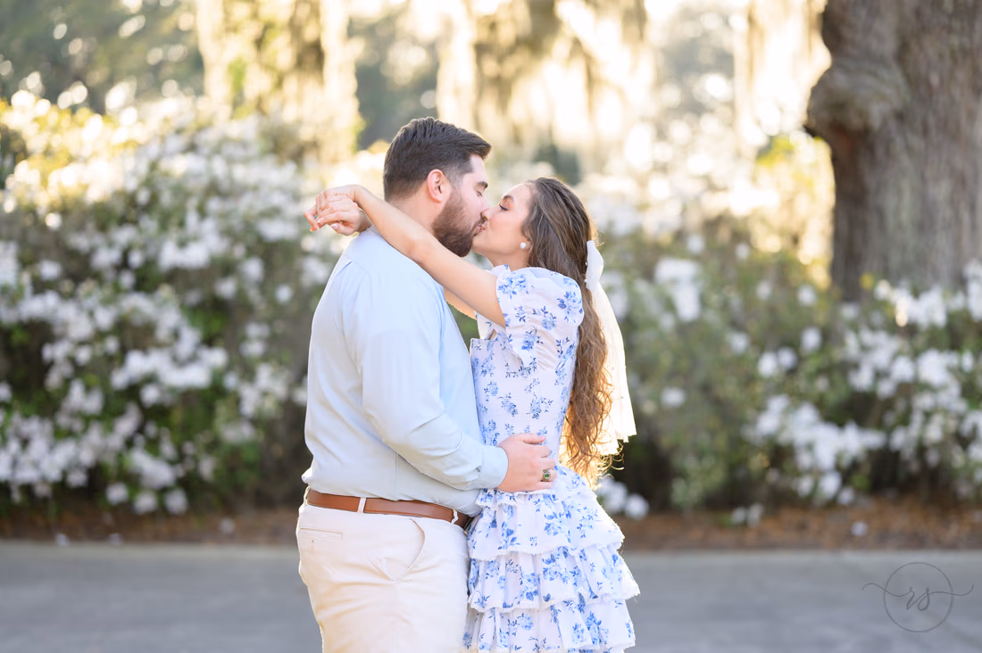 Couple kissing in front of white azaleas and a mossy oak at Caledonia Golf and Fish Club
