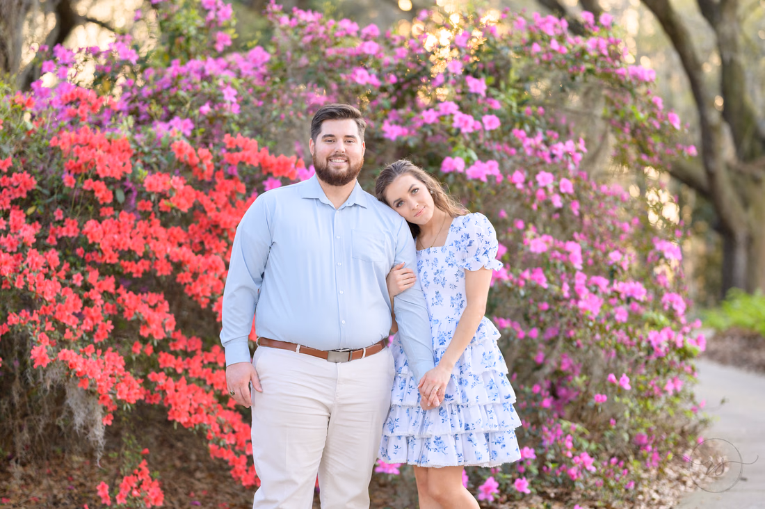Engaged couple standing in front of red and purple azaleas at Caledonia Golf and Fish Club