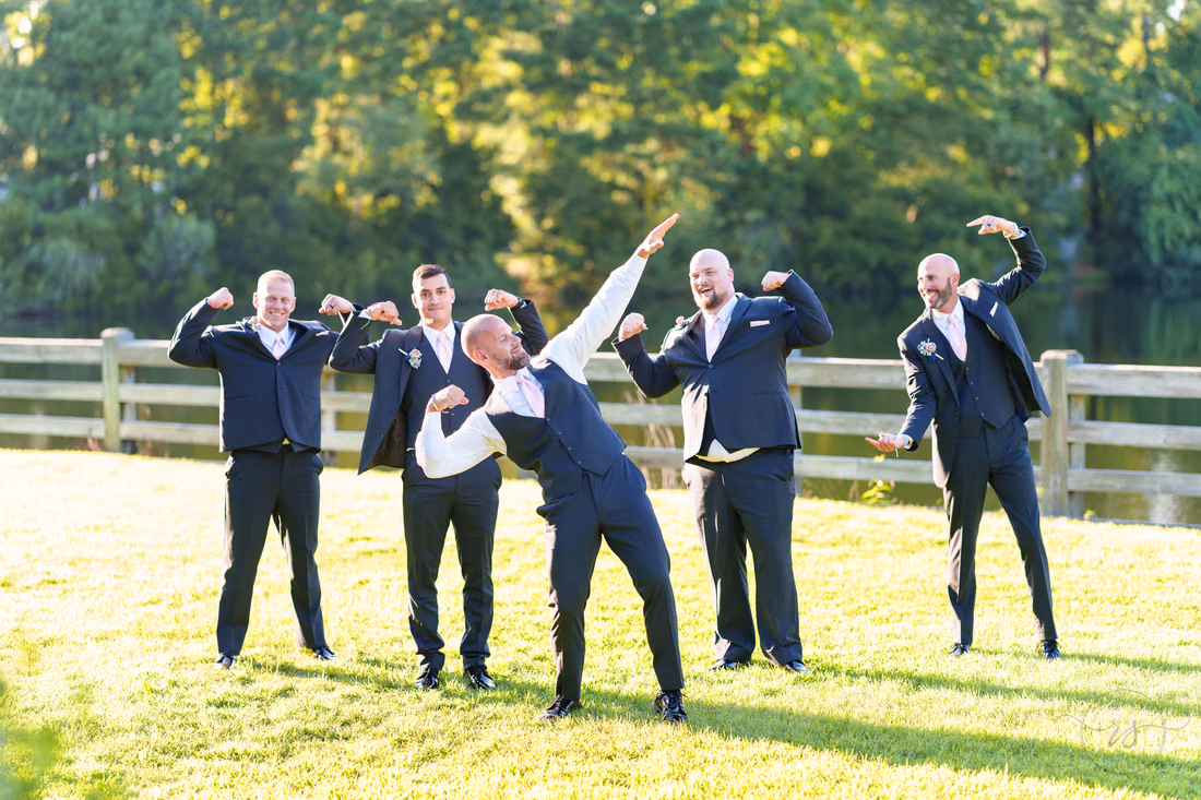 Groom and groomsmen striking playful bodybuilding poses by the fence - The Pavilion at Pepper Plantation