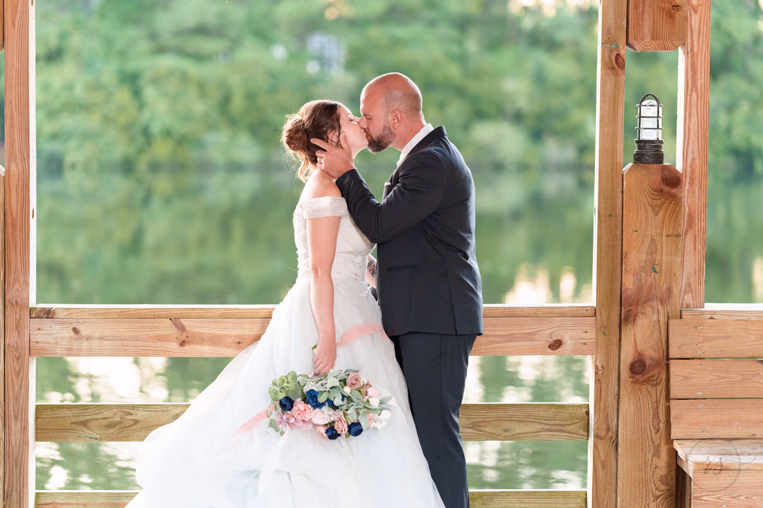 Bride and groom kissing in the lakeside gazebo with the lake behind them - The Pavilion at Pepper Plantation