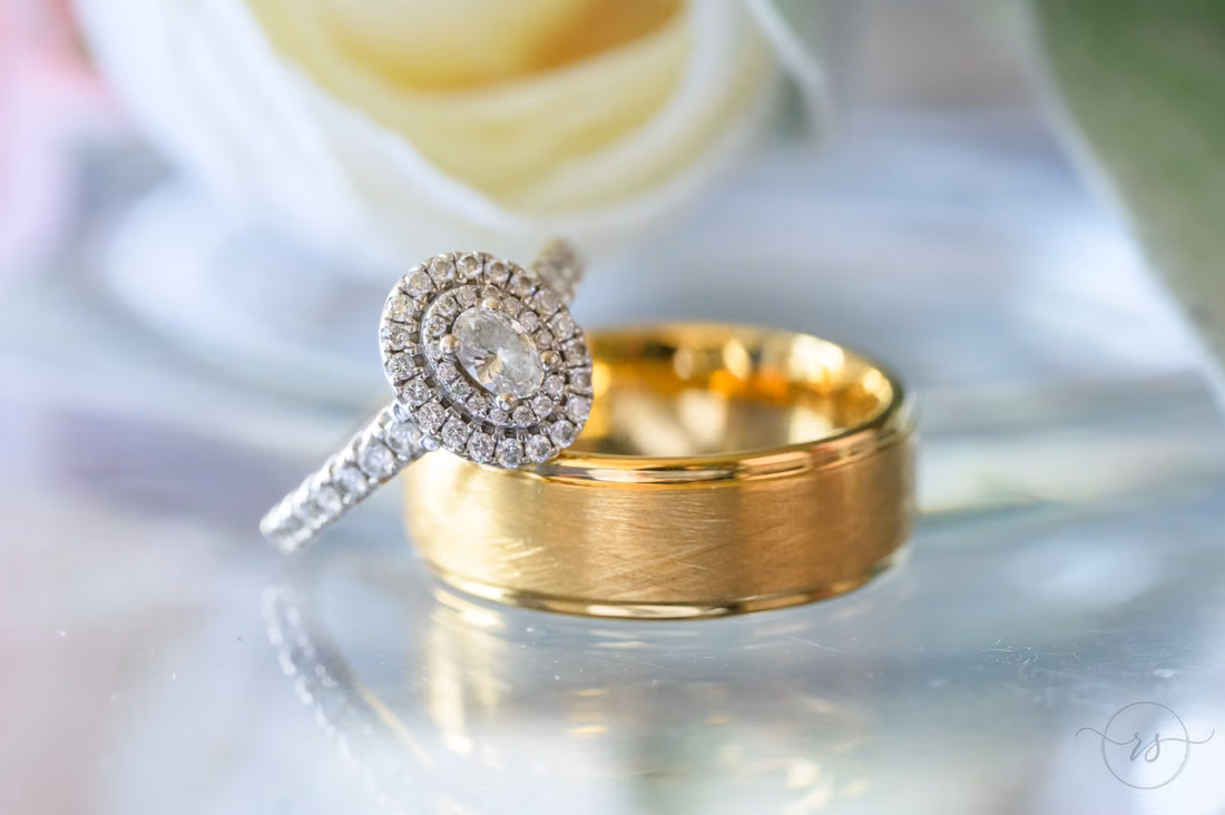 Oval halo engagement ring resting on the groom's gold band - Hotel Indigo