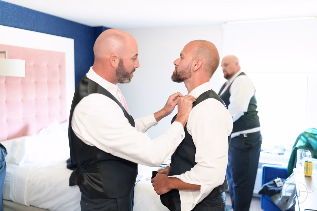Groom and groomsman helping each other with vests and ties - Hotel Indigo