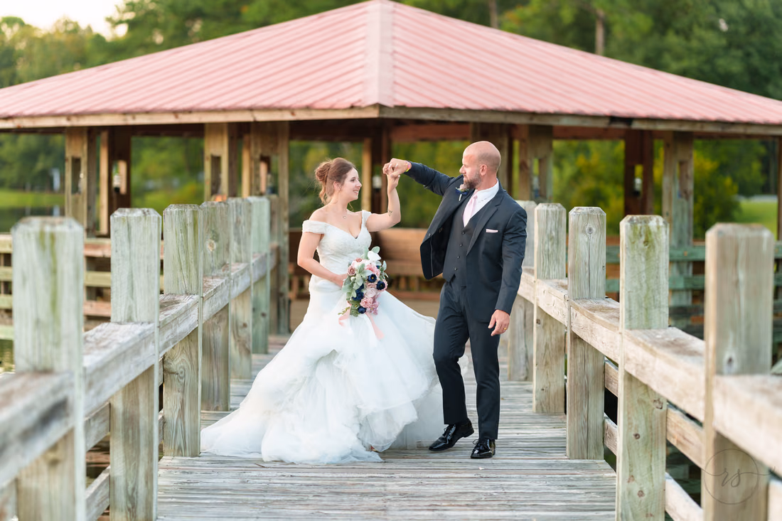 Groom twirling the bride on the boardwalk by the lakeside gazebo - The Pavilion at Pepper Plantation