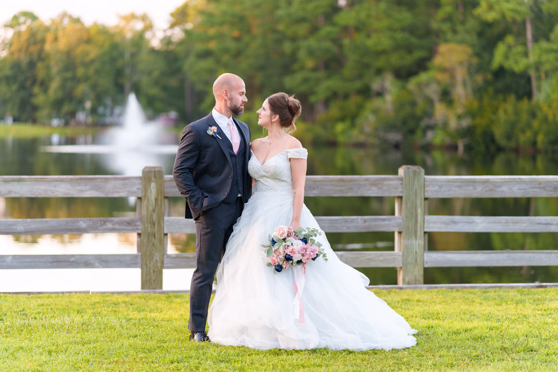 Groom gazing at the bride by the fence with the lake behind them - The Pavilion at Pepper Plantation