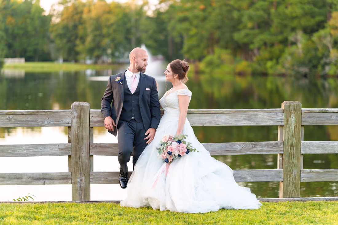 Groom sitting on the fence rail beside the bride at the lake - The Pavilion at Pepper Plantation