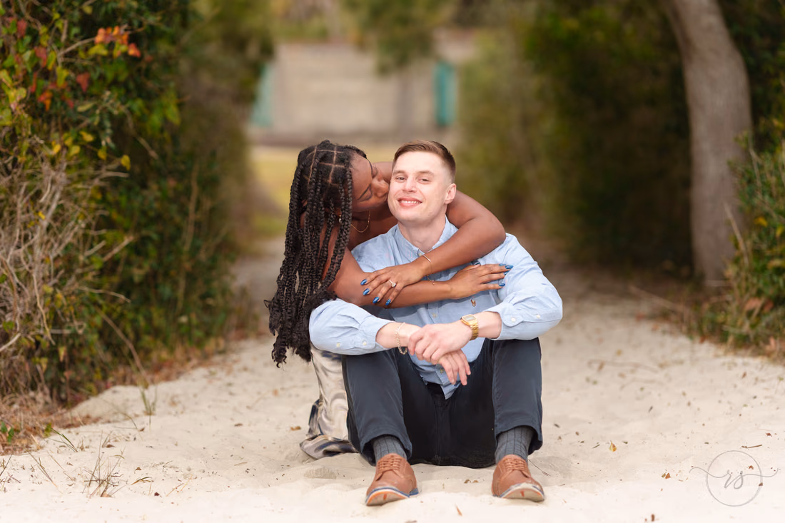 She hugs him from behind and kisses his cheek on the beach path - Huntington Beach State Park