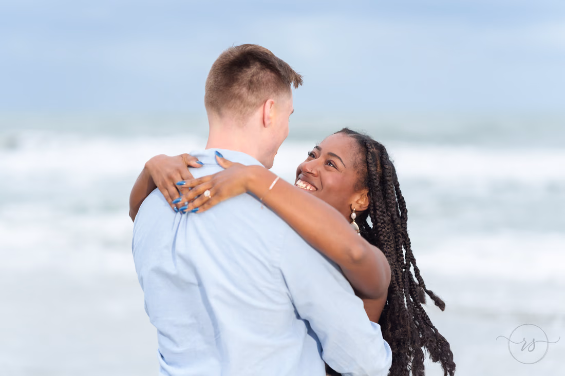 She smiles over his shoulder as they hug by the ocean - Huntington Beach State Park