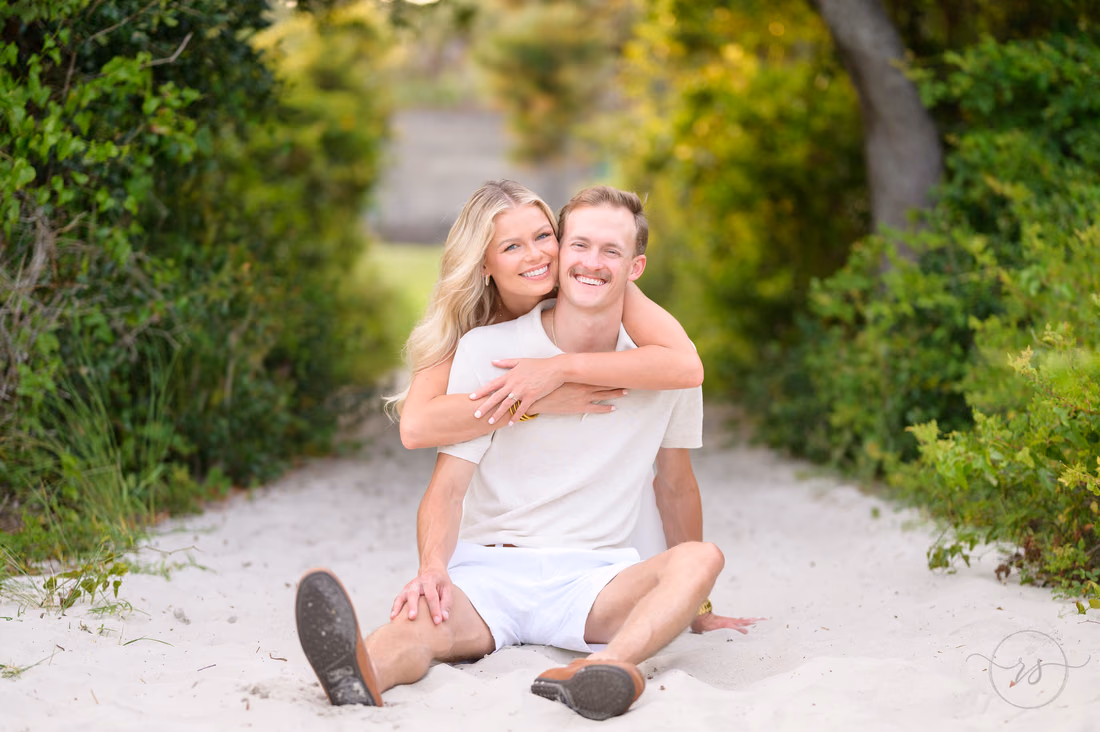 She hugs him from behind as they sit on the beach path - Huntington Beach State Park