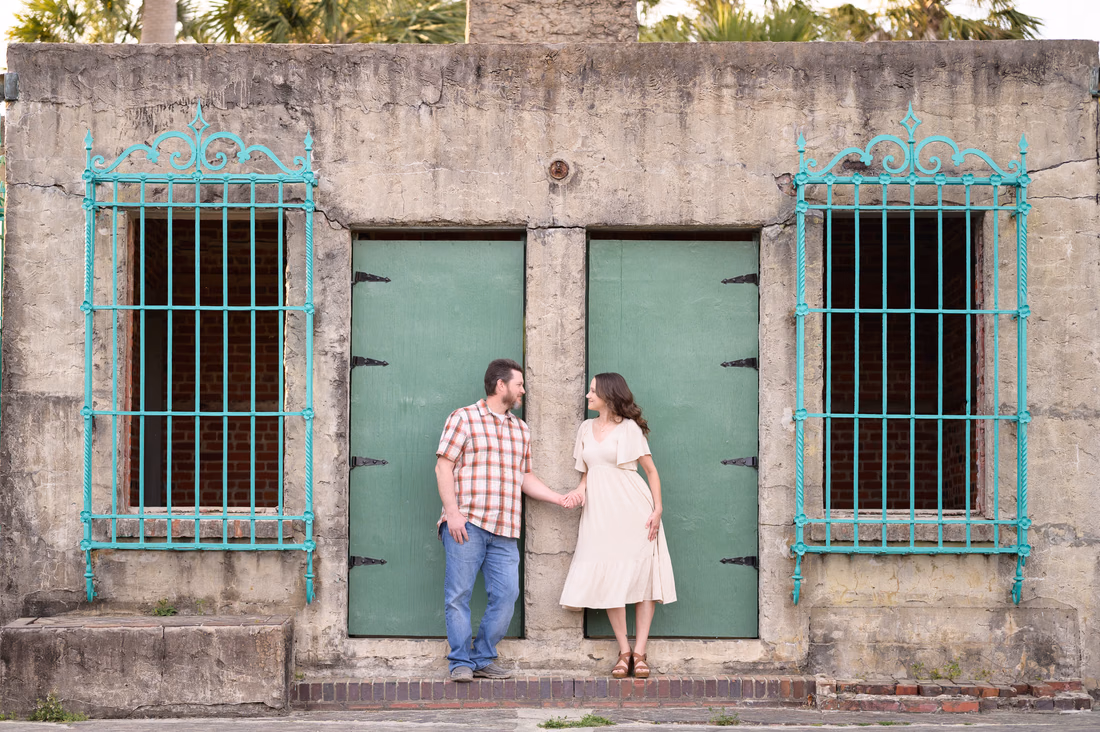 Couple holding hands in front of the green doors and iron windows of Atalaya Castle - Huntington Beach State Park