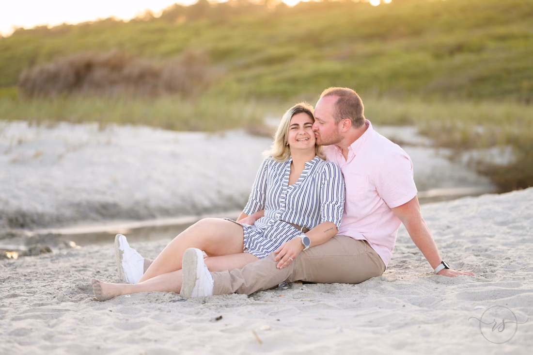 He kisses her cheek as they sit on the sand by the dunes - Myrtle Beach State Park