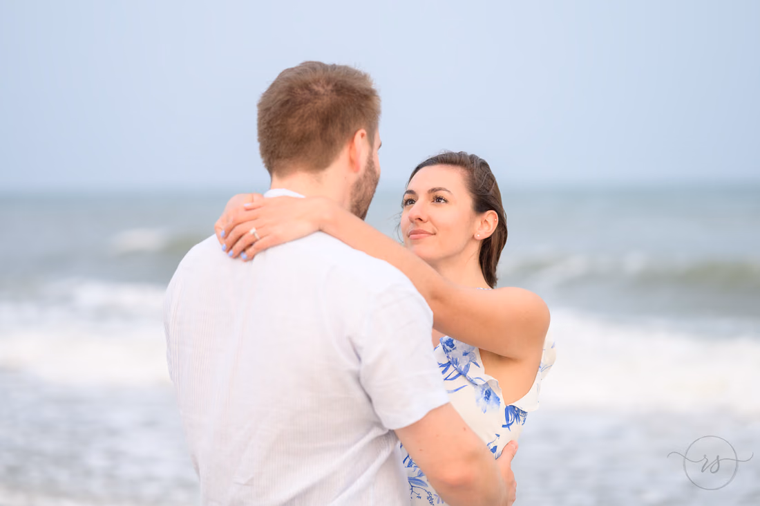 She smiles over his shoulder as they hug by the ocean - Huntington Beach State Park