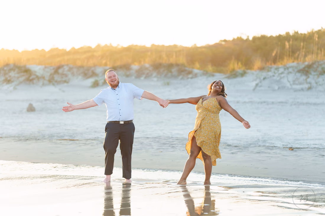 Couple holding hands with arms out at the water's edge - Huntington Beach State Park