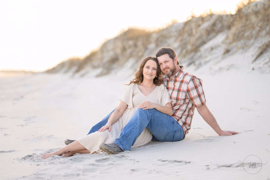 Couple sitting together on the sand in front of the dunes - Huntington Beach State Park