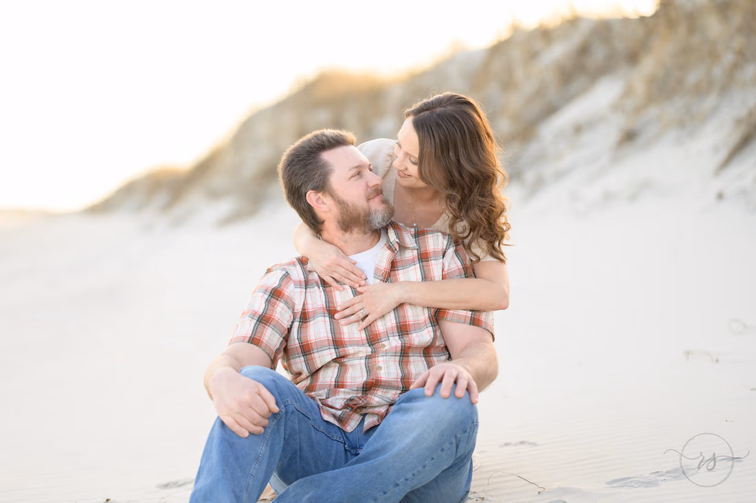 She hugs him from behind as they sit by the dunes - Huntington Beach State Park