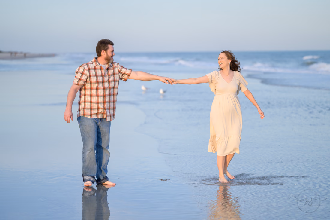 Couple reaching for each other's hands as they walk through the shallow water - Huntington Beach State Park