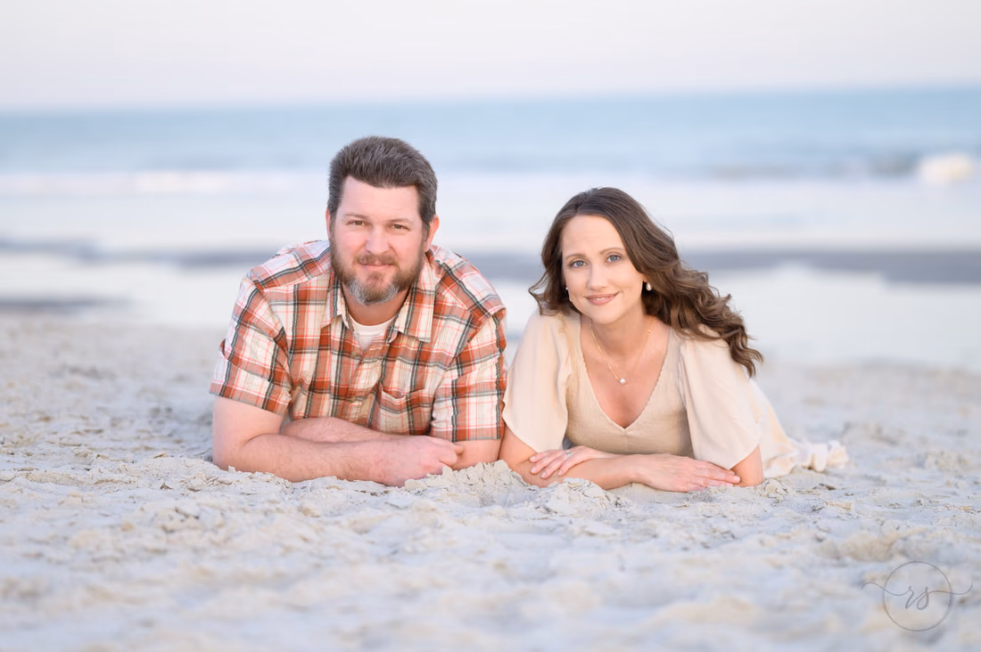 Couple lying on the sand smiling at the camera - Huntington Beach State Park