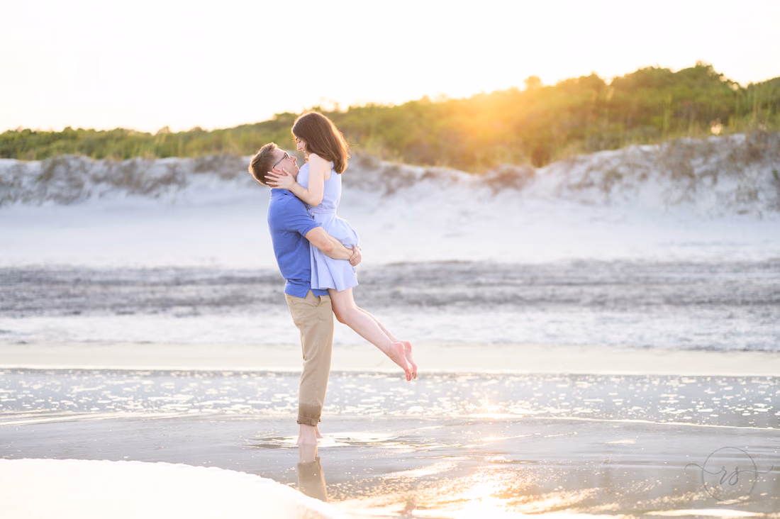 He lifts her for a kiss as the sun sets behind the dunes - Huntington Beach State Park