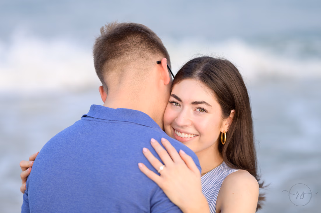 She smiles over his shoulder, showing her engagement ring - Huntington Beach State Park