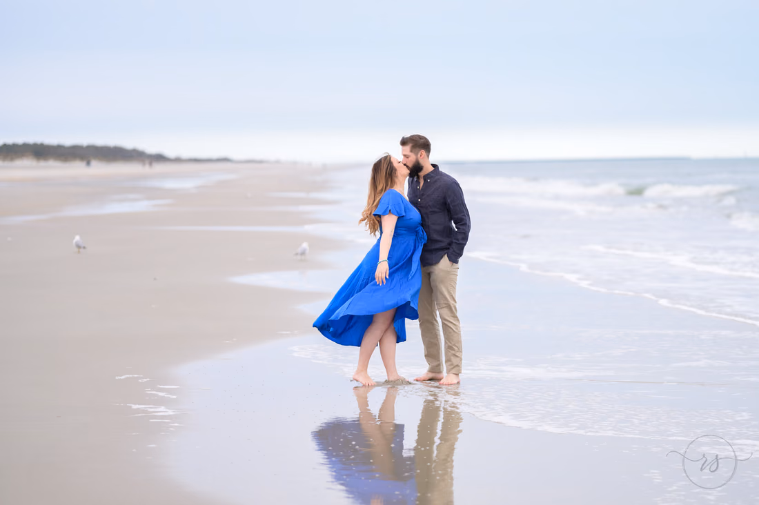 Couple kissing at the water's edge, her blue dress blowing in the wind - Huntington Beach State Park