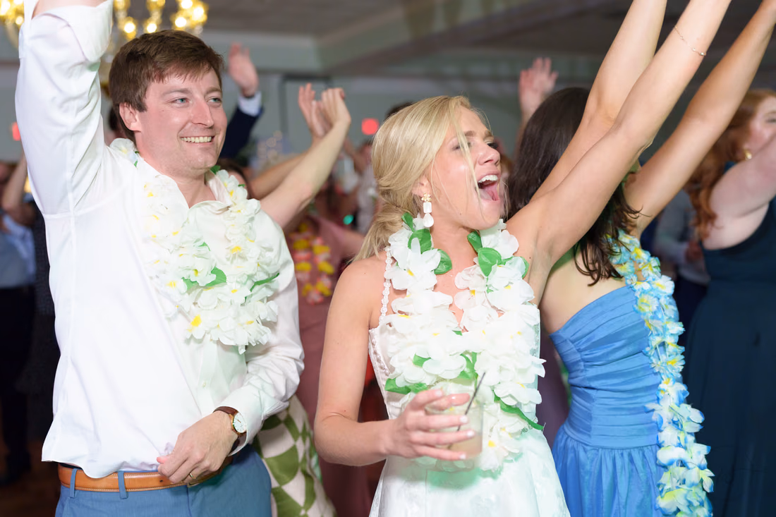 Bride and groom in leis cheer with their arms up on the dance floor at Pawleys Plantation