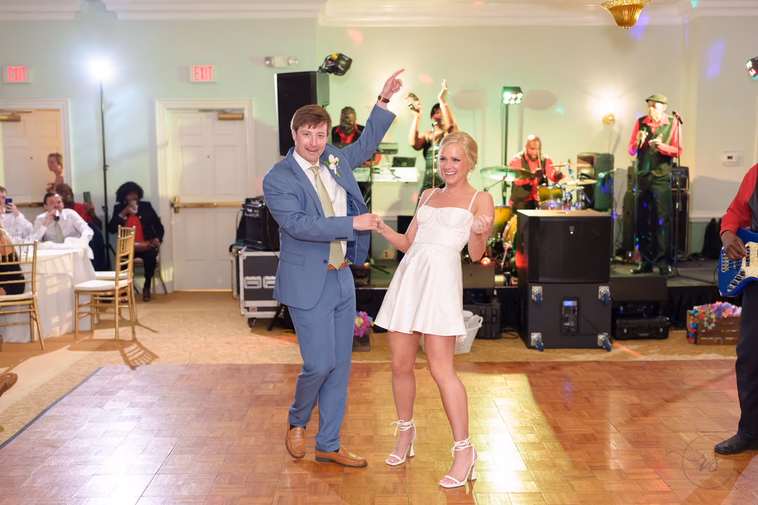 Bride in a short reception dress dances with the groom in front of the band at Pawleys Plantation