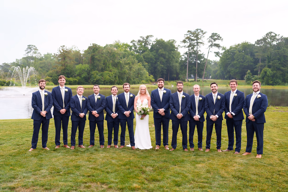 Bride with the groom's twelve groomsmen in navy suits by the fountain pond at Pawleys Plantation