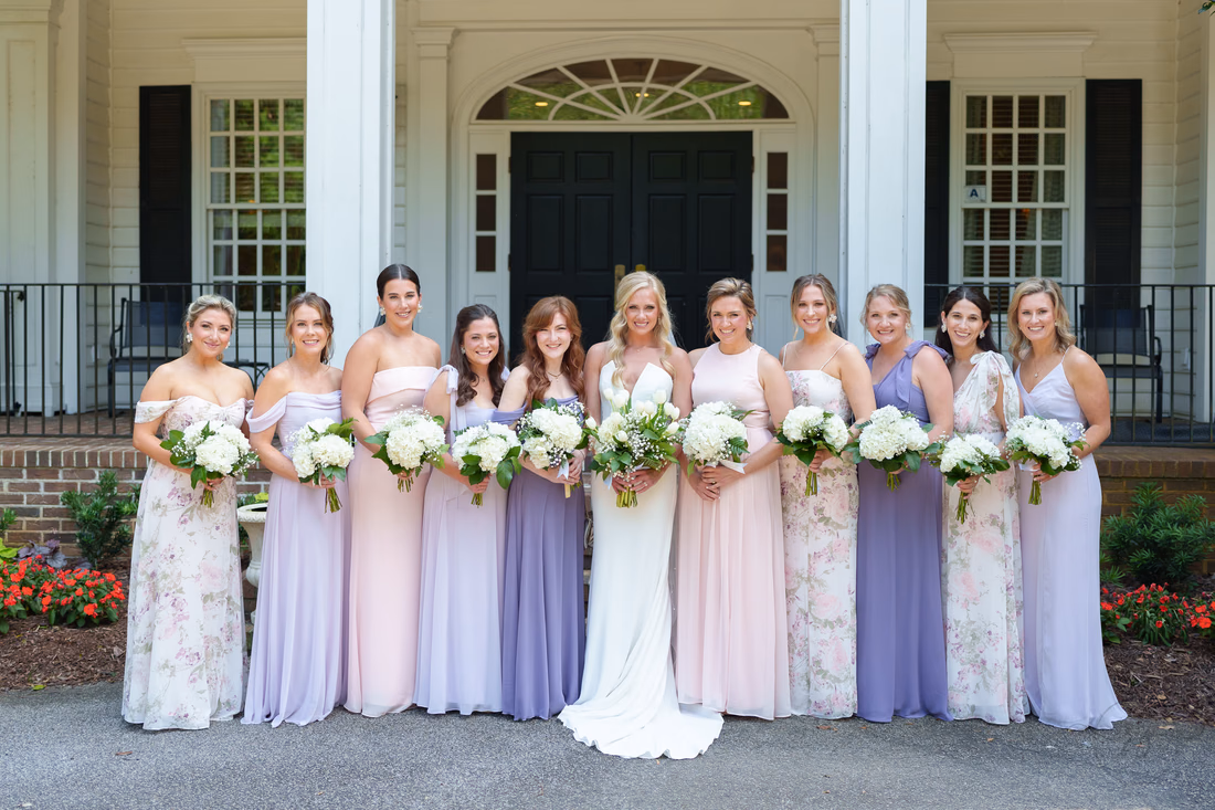 Bride lined up with her ten bridesmaids in lavender, pink and floral dresses at Pawleys Plantation