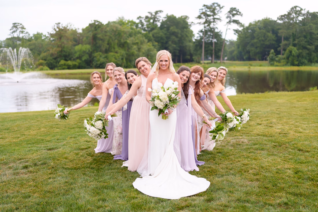 Bridesmaids lean out from behind the bride in a line on the lawn at Pawleys Plantation