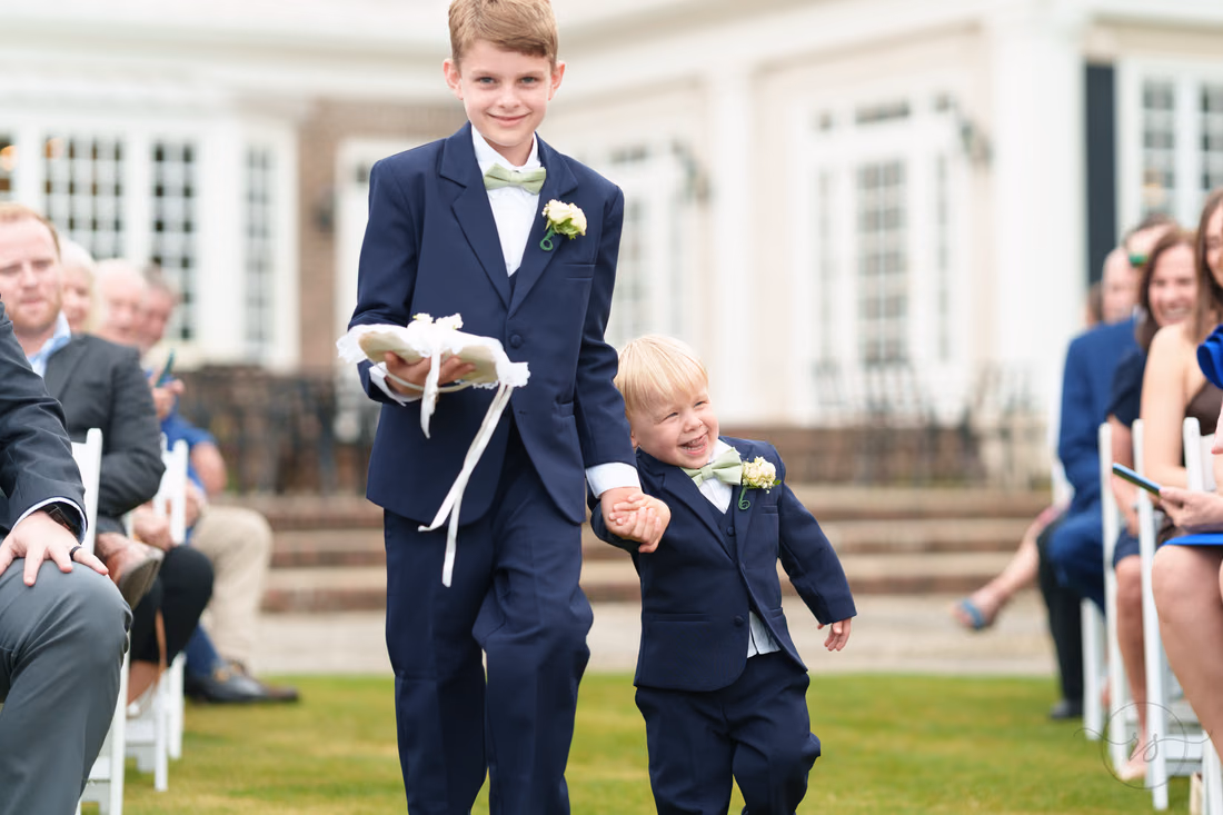 Older ring bearer carries the ring pillow and holds a toddler's hand in the aisle at Pawleys Plantation