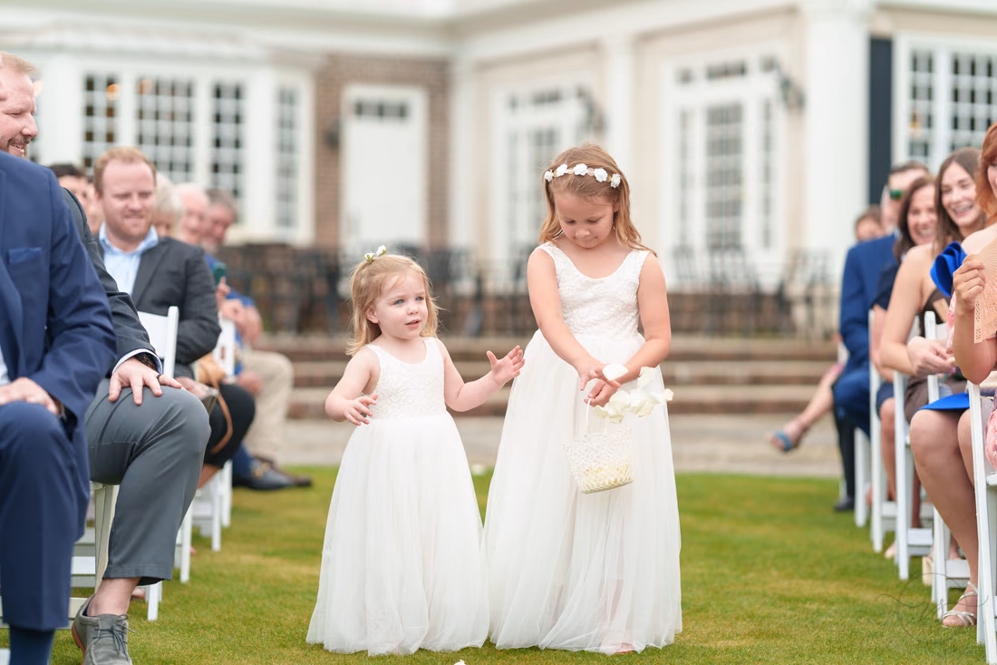 Two flower girls in white dresses walk down the aisle at Pawleys Plantation