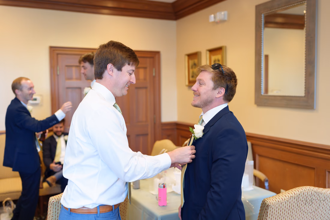 The groom pins a boutonniere on a groomsman in the getting-ready room at Pawleys Plantation