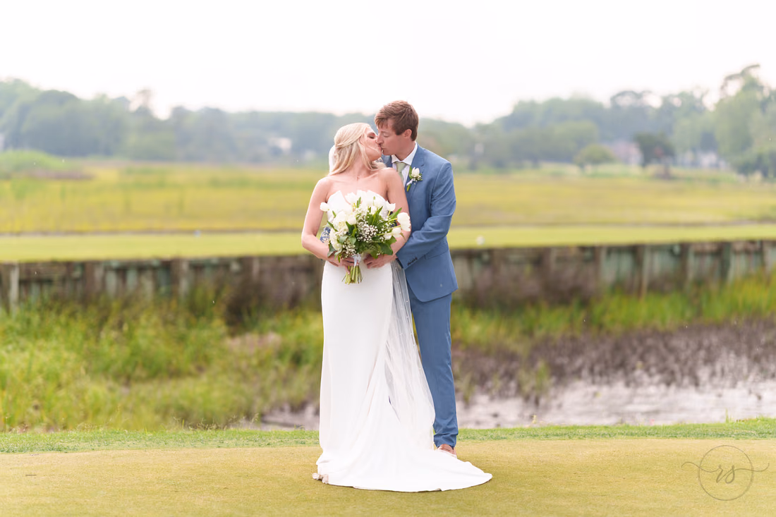 Groom kisses the bride's forehead on the green beside the marsh at Pawleys Plantation