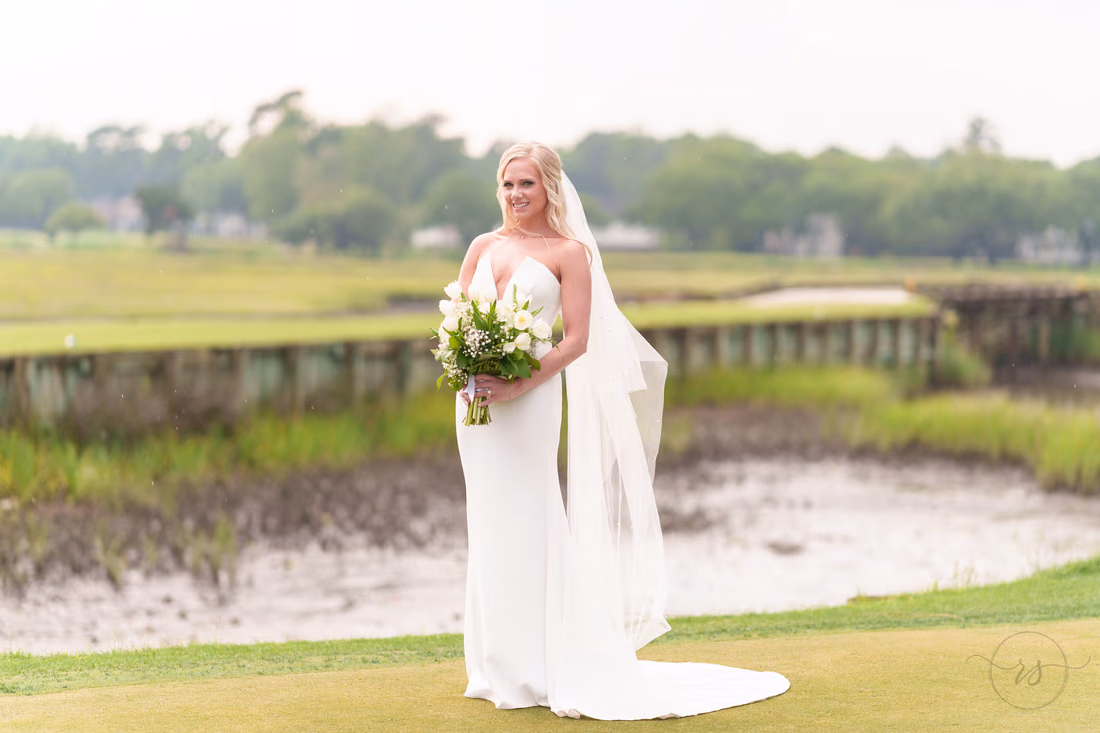 Bride holds her bouquet on the green by the marsh on a rainy afternoon at Pawleys Plantation