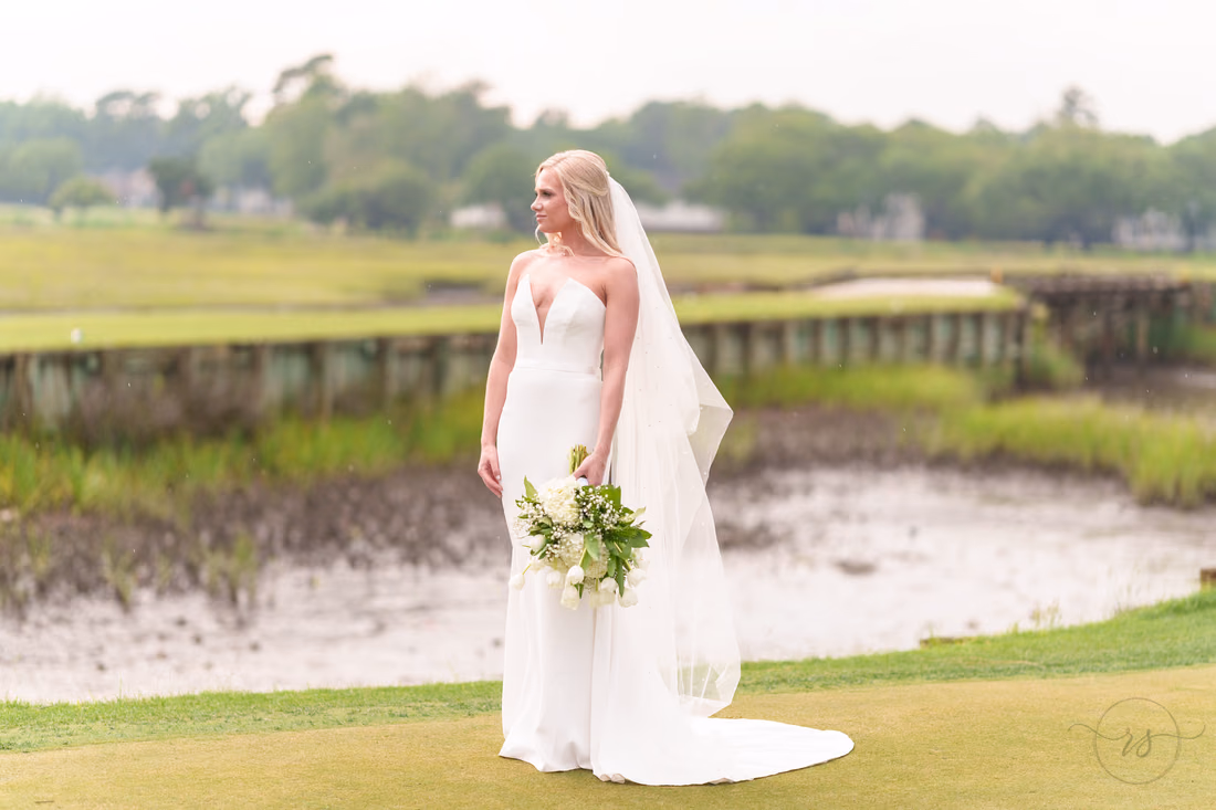 Bride looks over her shoulder with her veil trailing on the green at Pawleys Plantation