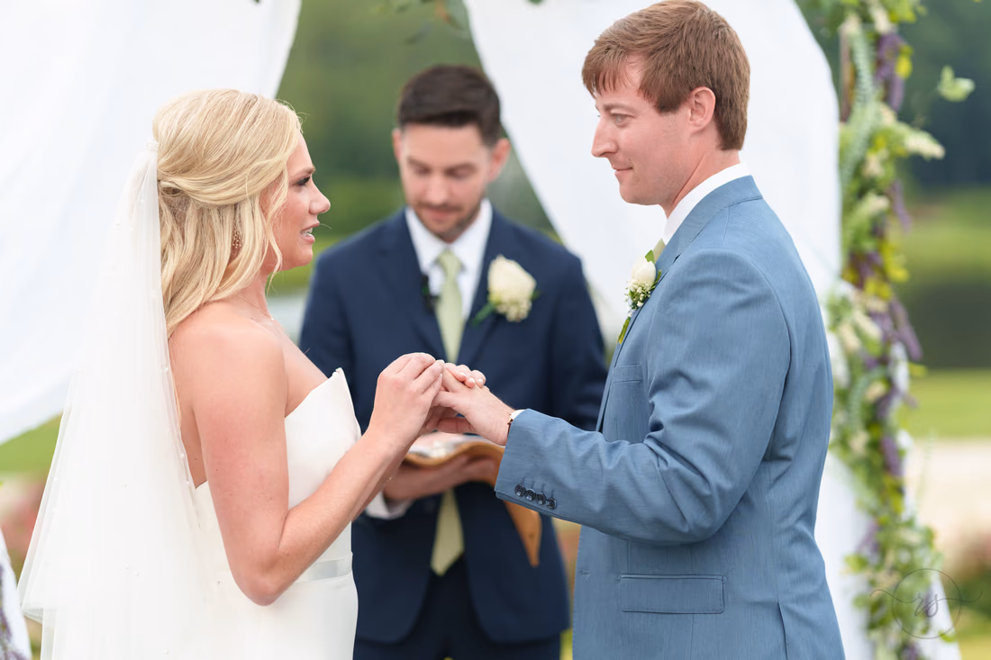 Bride and groom smile as they exchange rings under the floral arch at Pawleys Plantation