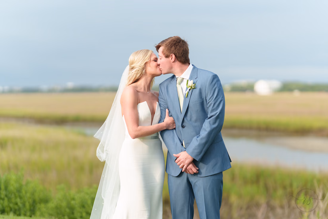 Bride kisses the groom on the cheek in front of the marsh as the sun comes out at Pawleys Plantation