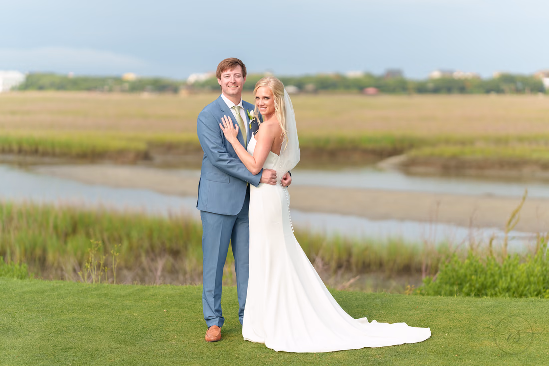 Bride and groom embrace and smile on the golf course green by the marsh at Pawleys Plantation