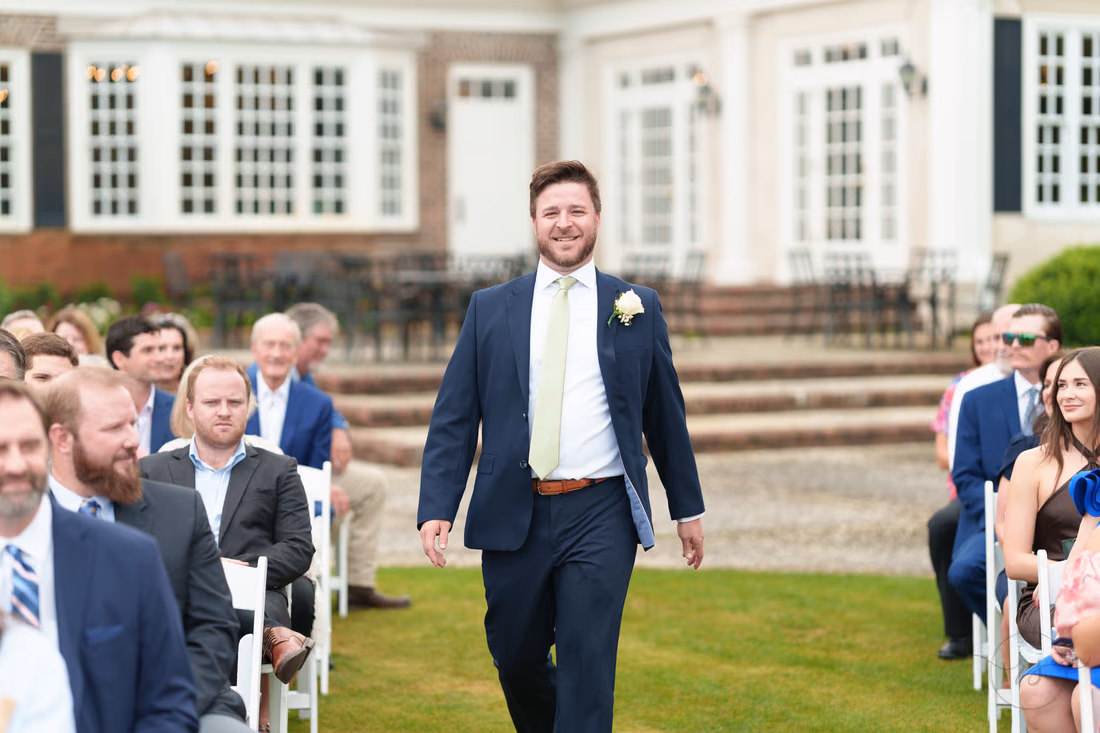 Groomsman smiles as he walks down the aisle on the lawn at Pawleys Plantation