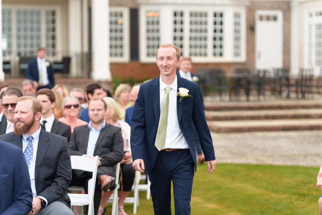 Groomsman in a navy suit walks down the aisle past the guests at Pawleys Plantation
