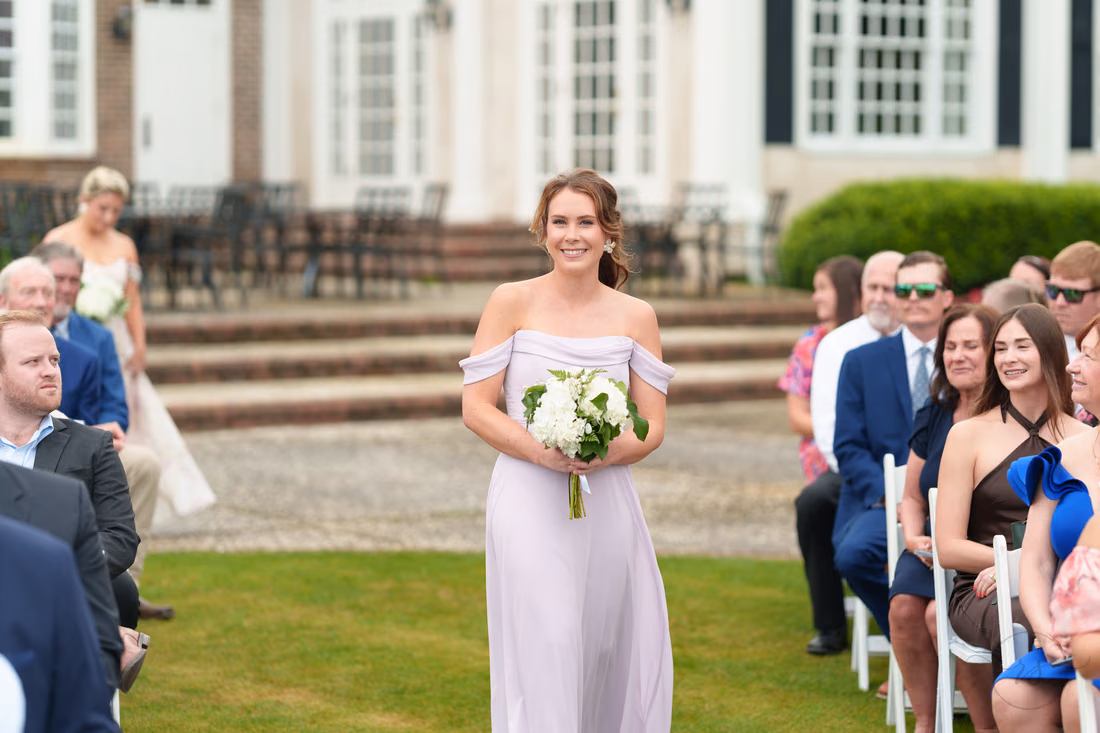 Bridesmaid in lilac walks down the aisle with her bouquet at Pawleys Plantation